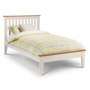 A full shot of the Salerno Shaker Bed, showing its two-tone finish with an ivory lacquer frame and solid white oak cappings on the headboard and footboard. The bed is styled with white bedding in a bedroom with a dark blue feature wall.