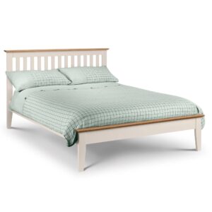 A full shot of the Salerno Shaker Bed, showing its two-tone finish with an ivory lacquer frame and solid white oak cappings on the headboard and footboard. The bed is styled with white bedding in a bedroom with a dark blue feature wall.