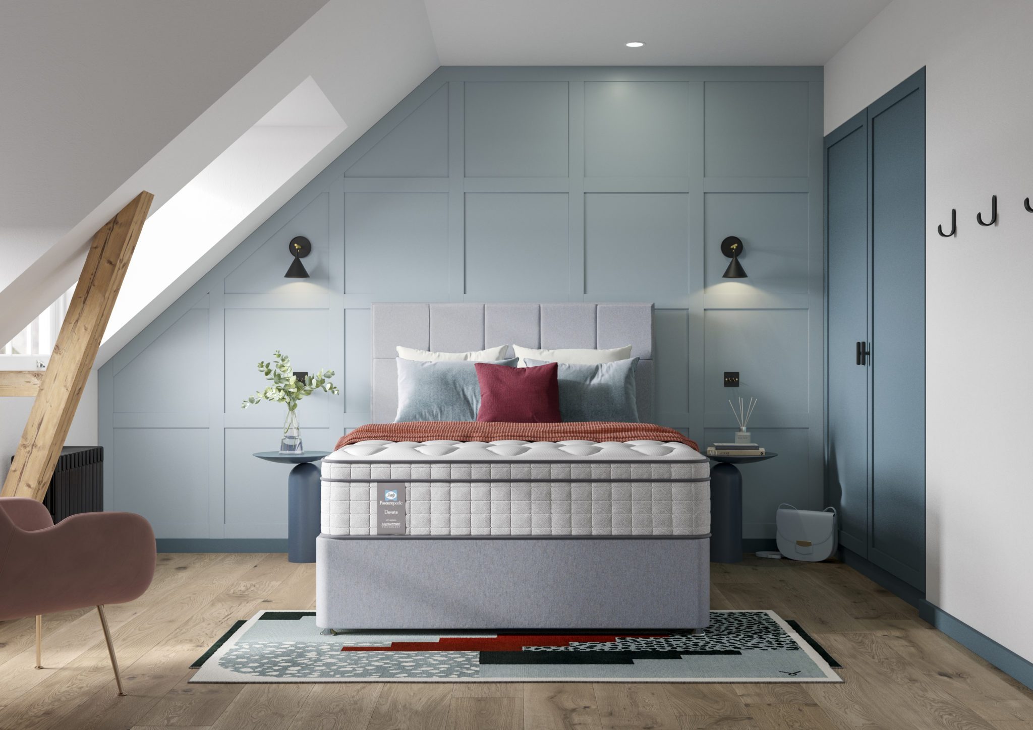 A full shot of the Blake Medium Mattress, shown on a light grey divan base with a matching upholstered headboard, set in a contemporary bedroom with light blue wall panelling. The mattress has a deep quilted white top.