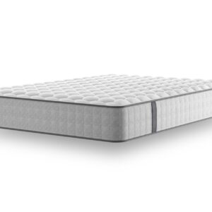 A full shot of the Emin Firm Mattress, shown on a dark grey divan base with a matching headboard, set in a contemporary bedroom with a brick feature wall. The mattress has a classic quilted white top.