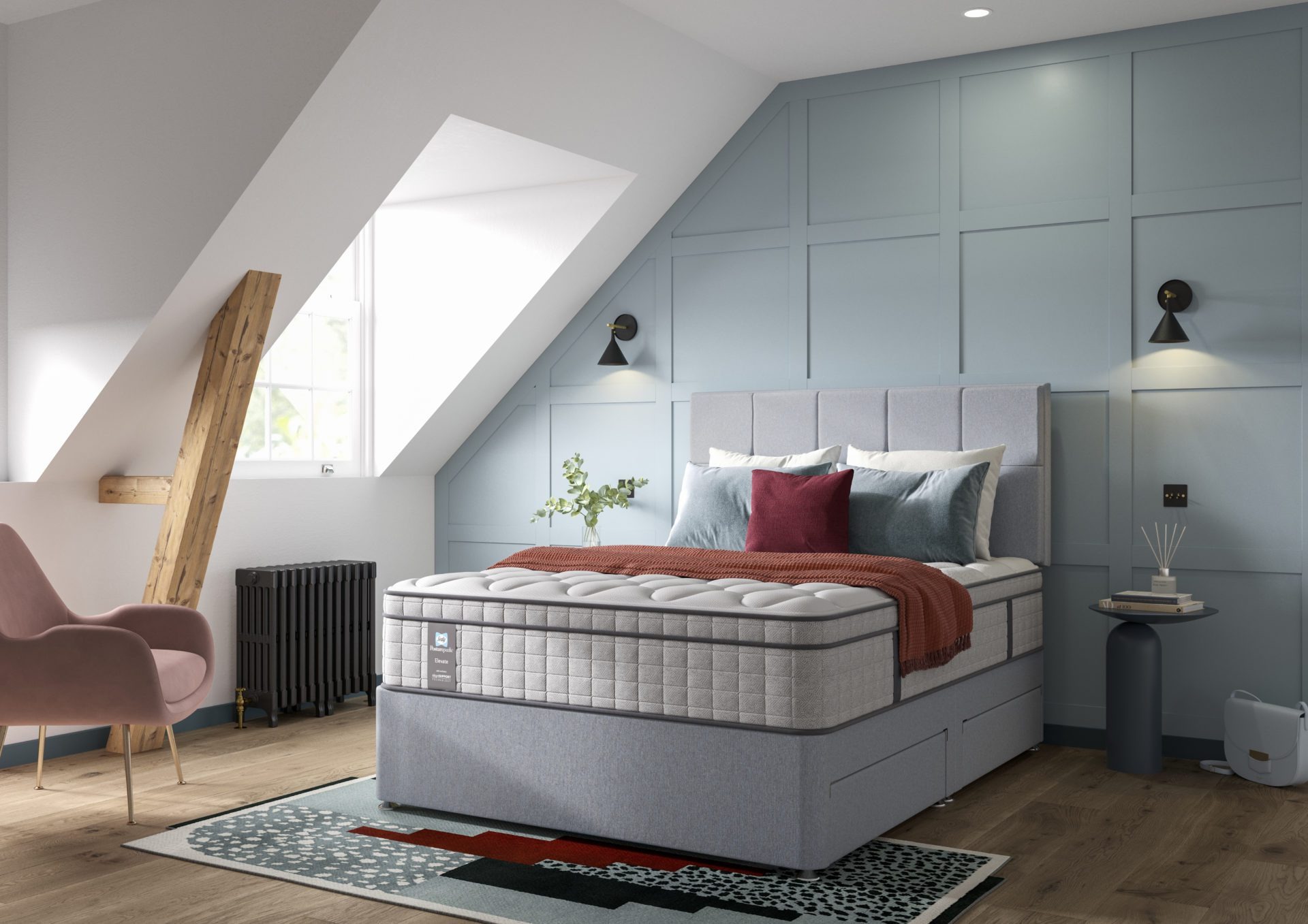 A full shot of the Blake Medium Mattress, shown on a light grey divan base with a matching upholstered headboard, set in a contemporary bedroom with light blue wall panelling. The mattress has a deep quilted white top.
