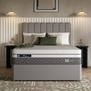 A full shot of the Hydra 2300 Hybrid Mattress, shown on a light grey divan base with drawers and a curved upholstered headboard, set in a contemporary bedroom. The mattress features a white top panel and a distinctive grey quilted side panel.