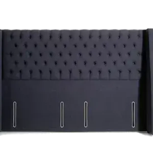 A deeply-buttoned, winged, and extra-wide headboard with wrap-around side wings and piped detail, shown in a dark blue upholstered fabric. The headboard is shown against a plain grey background.